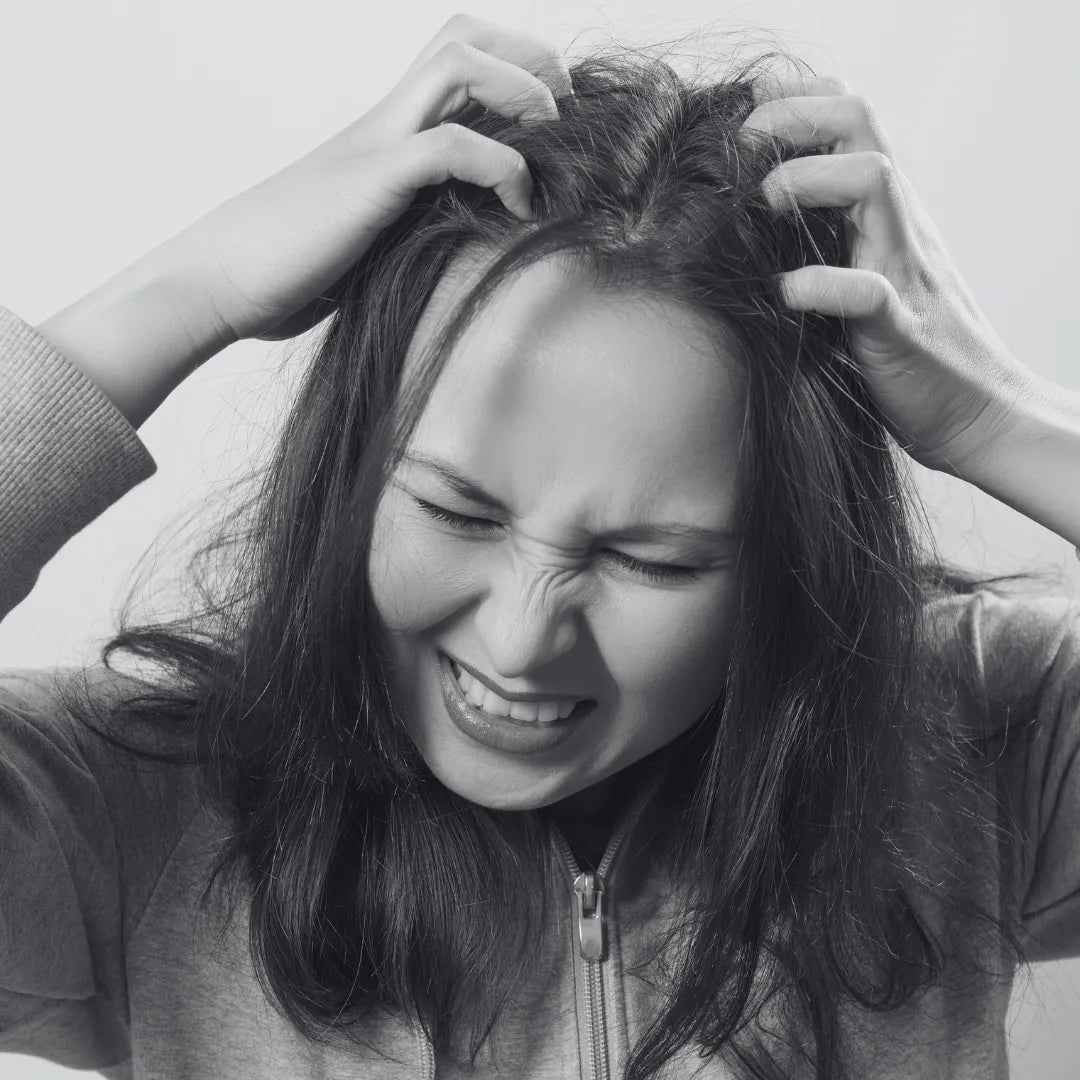 A black and white image of a young girl scratching her head because of dandruff. for this we have Herbstonic All In One Hair Oil.