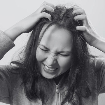 A black and white image of a young girl scratching her head because of dandruff. for this we have Herbstonic All In One Hair Oil. 